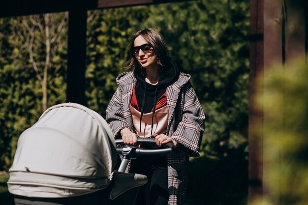 Joven madre caminando con carro de bebé en el parque