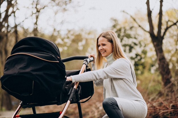 Joven madre caminando con carro de bebé en el parque