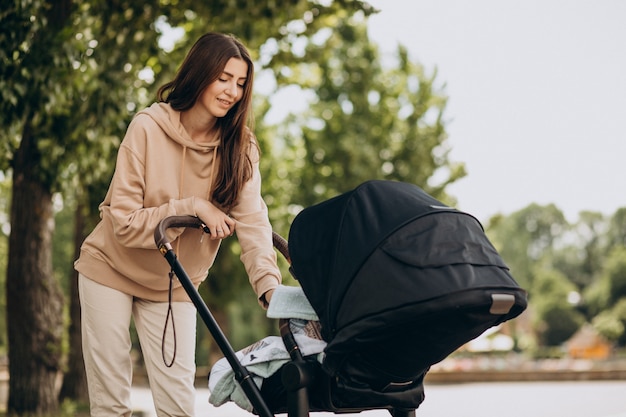 Joven madre caminando con carro de bebé en el parque