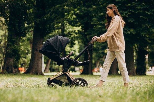 Joven madre caminando con carro de bebé en el parque