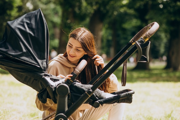 Joven madre caminando con carro de bebé en el parque