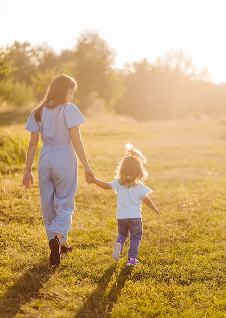 Joven madre e hija, abrazándose y jugando en un campo dorado de sol