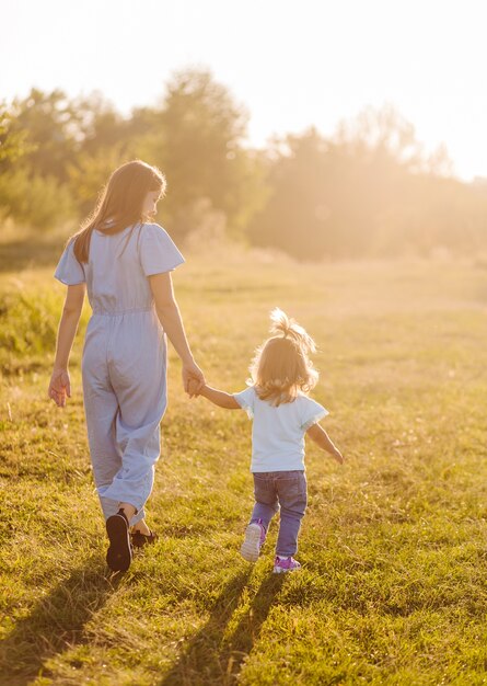 Joven madre e hija, abrazándose y jugando en un campo dorado de sol