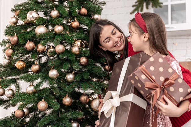 Joven madre e hija pequeña con un regalo de Navidad, el niño se regocija con el regalo de Navidad.