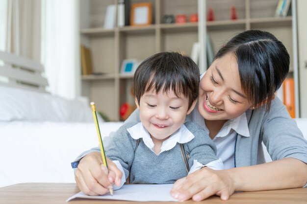 Joven madre enseñando a su hijo a escribir en papel con amor