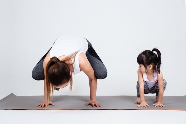 Joven madre entrenando encantadora hija con yoga