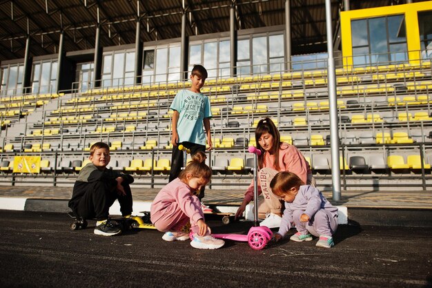 Foto gratuita joven madre con estilo con cuatro hijos al aire libre familia deportiva pasar tiempo libre al aire libre con scooters y patines pintado con tiza en el asfalto