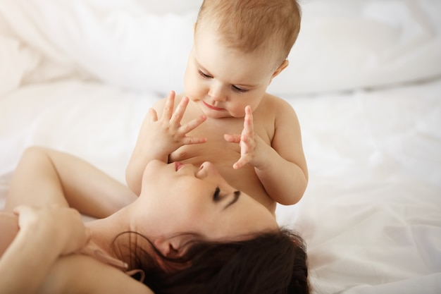 Joven madre feliz y su pequeña hija sonriente abrazando acostado en la cama en su casa.