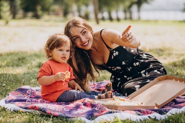 Joven madre hermosa con little baby boy comer pizza en el parque