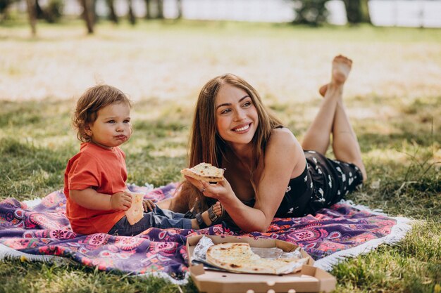 Joven madre hermosa con little baby boy comer pizza en el parque