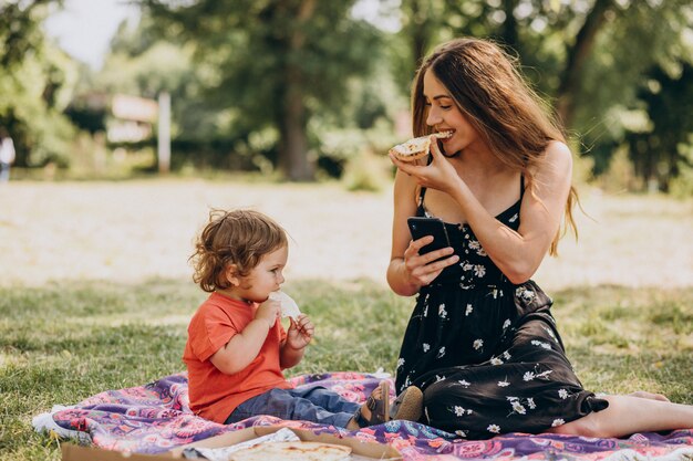 Joven madre hermosa con little baby boy comer pizza en el parque