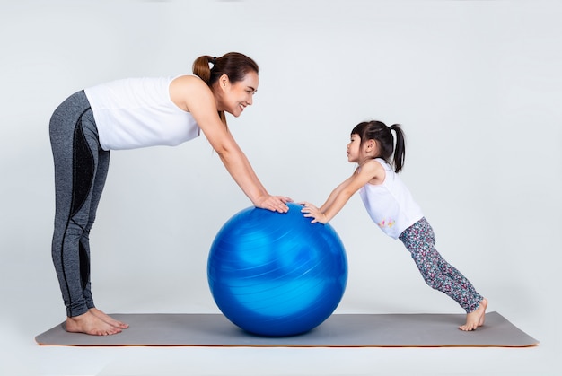 Joven madre con hija pequeña ejercicio en pelota fitness
