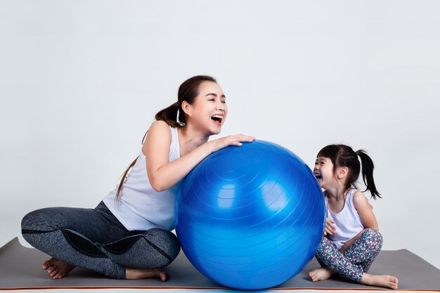Joven madre con hija pequeña ejercicio en pelota fitness