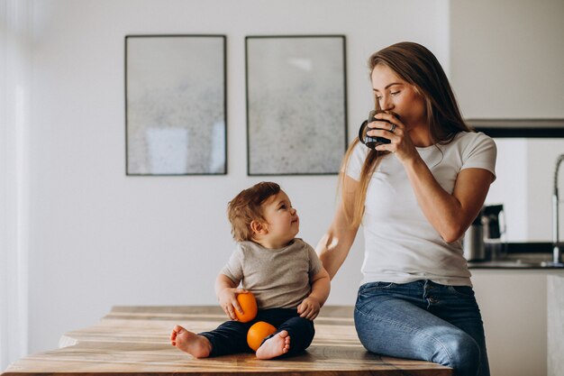 Joven madre con hijo pequeño bebiendo agua en casa