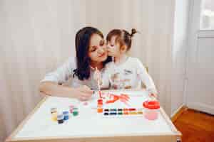 Foto gratuita una joven madre, junto con su pequeña hija pinta sobre papel