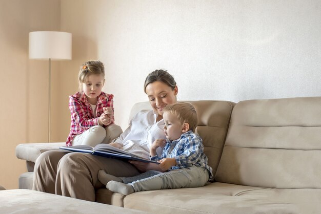 Joven madre leyendo un libro para sus hijos pequeños