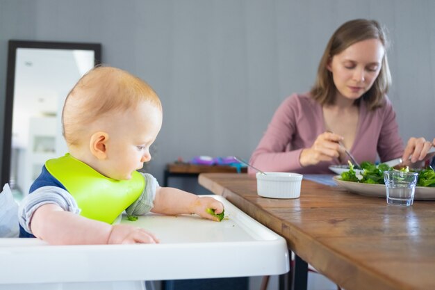 Joven madre y linda hija comiendo vegetales verdes