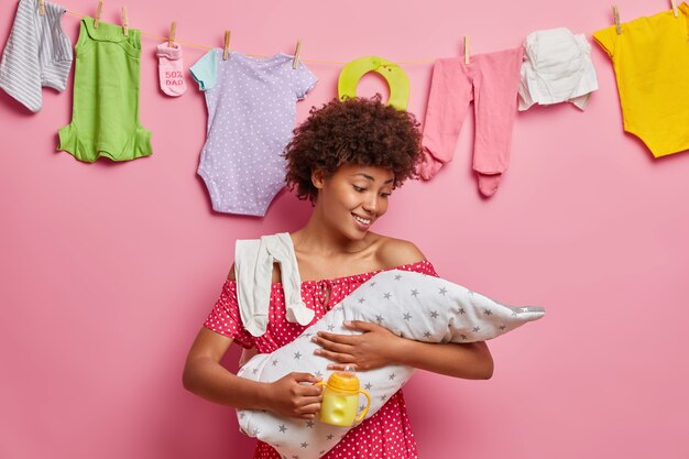 Joven madre solícita se preocupa por el recién nacido, se alimenta con leche, disfruta de momentos felices de maternidad, posa en casa. Bebé en alimentación artificial. Niñera, concepto de crianza de los hijos. Nacimiento de niño