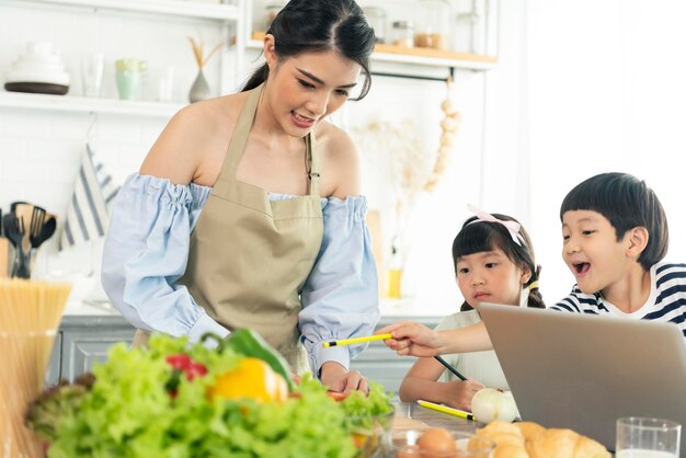 Joven madre soltera asiática haciendo comida mientras cuida a un niño en la cocina