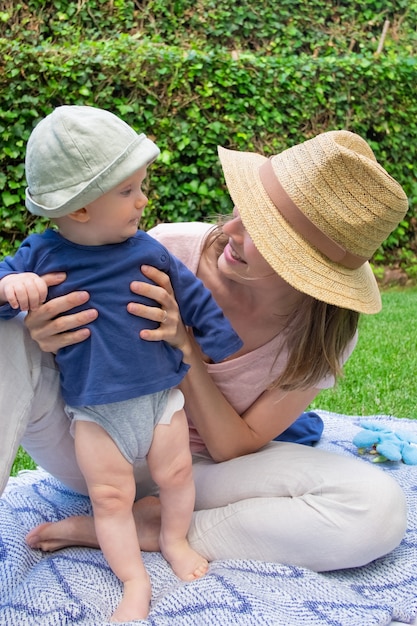 Joven madre con sombrero mirando a la hija y sonriendo