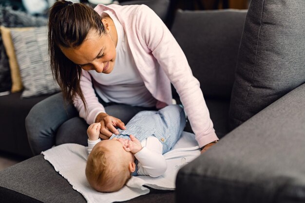 Joven madre sonriente cuidando a su bebé que está acostado en el sofá