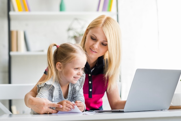 Joven madre con su hija feliz usando la computadora portátil en casa