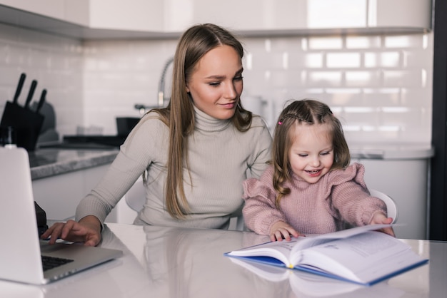 Joven madre y su hija hija haciendo tarea escribiendo y leyendo en casa