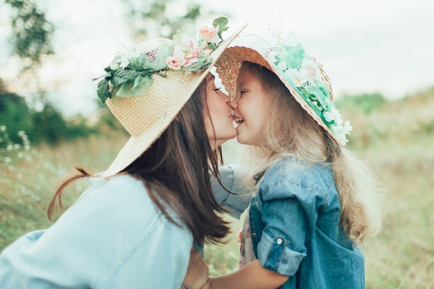 La joven madre y su hija con sombreros sobre la hierba verde
