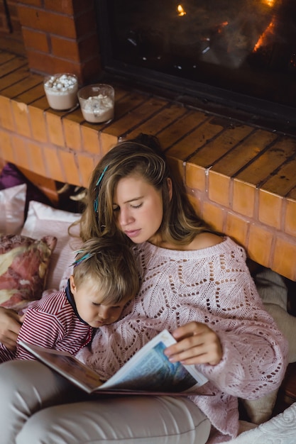 Una joven madre y su hijo están leyendo un libro de cuento de hadas cerca de la chimenea.
