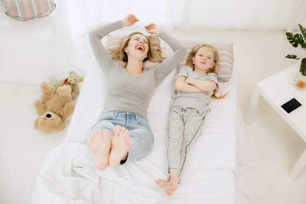 Joven madre y su pequeña hija en casa por la mañana soleada. Colores pastel suaves. Tiempo en familia feliz el fin de semana. Concepto del día de la madre. Conceptos de familia, amor, estilo de vida, maternidad y momentos tiernos.