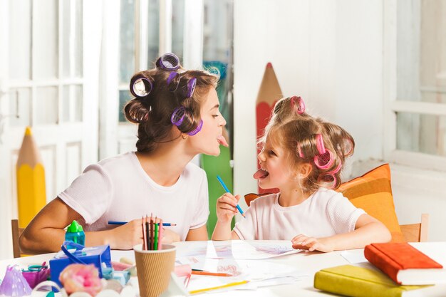 La joven madre y su pequeña hija dibujando con lápices en casa