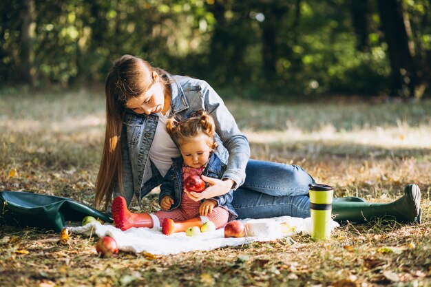 Joven madre con su pequeña hija en un parque de otoño con picnic