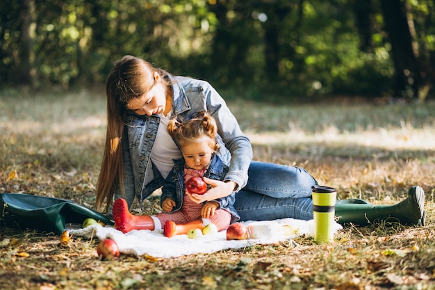 Joven madre con su pequeña hija en un parque de otoño con picnic