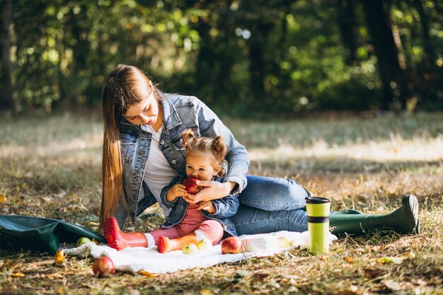 Joven madre con su pequeña hija en un parque de otoño con picnic