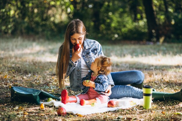 Joven madre con su pequeña hija en un parque de otoño con picnic