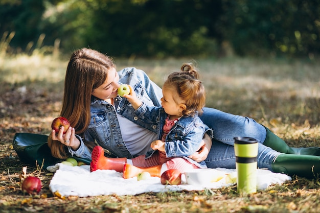 Joven madre con su pequeña hija en un parque de otoño con picnic