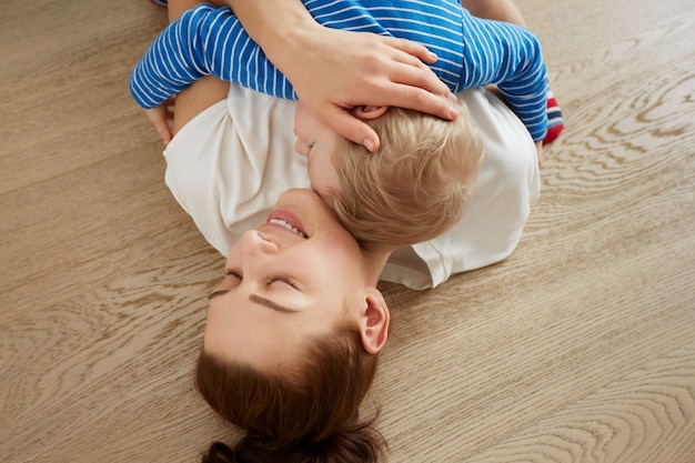 Foto gratuita joven madre con su pequeño hijo de un año vestido con pijama se está relajando y abrazándose