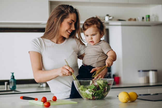 Foto gratuita joven madre con su pequeño hijo haciendo ensalada en la cocina