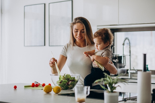 Foto gratuita joven madre con su pequeño hijo haciendo ensalada en la cocina