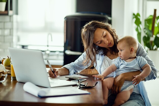 Joven madre trabajadora que planifica el presupuesto del hogar mientras está con su bebé en casa