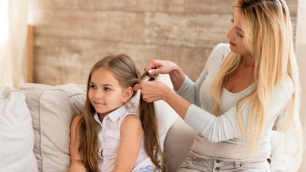 Joven madre trenzando el cabello de su hija