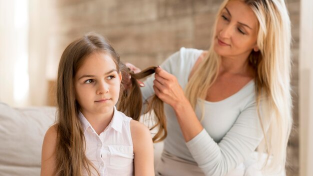 Joven madre trenzando el cabello de sus hijas en casa