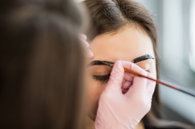 Foto gratuita joven maestro hace contornos de cejas para modelo bastante joven