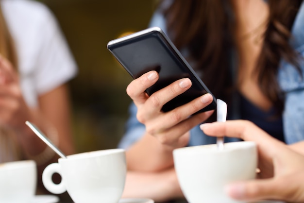 Joven mano con dispositivo moderno smartphone en la barra de café