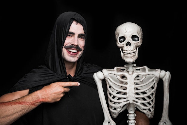 Foto gratuita joven en manto negro apuntando al esqueleto