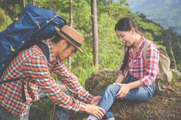 Un joven masajeando las piernas de su novia, que dolor en la cima de la colina en un bosque tropical, aventura de trekking.