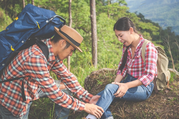 Un joven masajeando las piernas de su novia, que dolor en la cima de la colina en un bosque tropical, aventura de trekking.