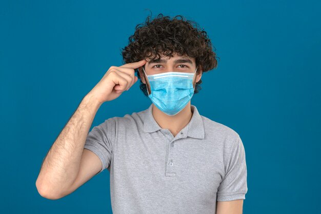 Foto gratuita joven con máscara protectora médica apuntando al templo con el dedo pensando centrado en una tarea sobre fondo azul aislado