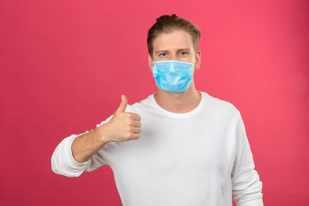 Foto gratuita joven en máscara protectora médica mirando a la cámara mostrando los pulgares para arriba sobre fondo rosa aislado