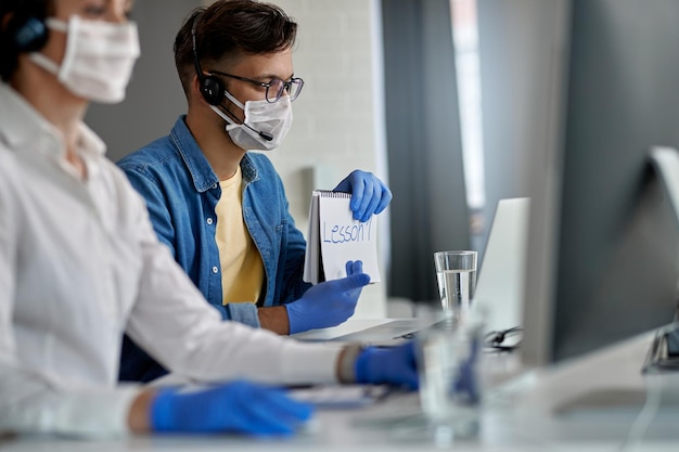 Joven con mascarilla protectora mientras imparte clases en línea por computadora durante la epidemia de coronavirus